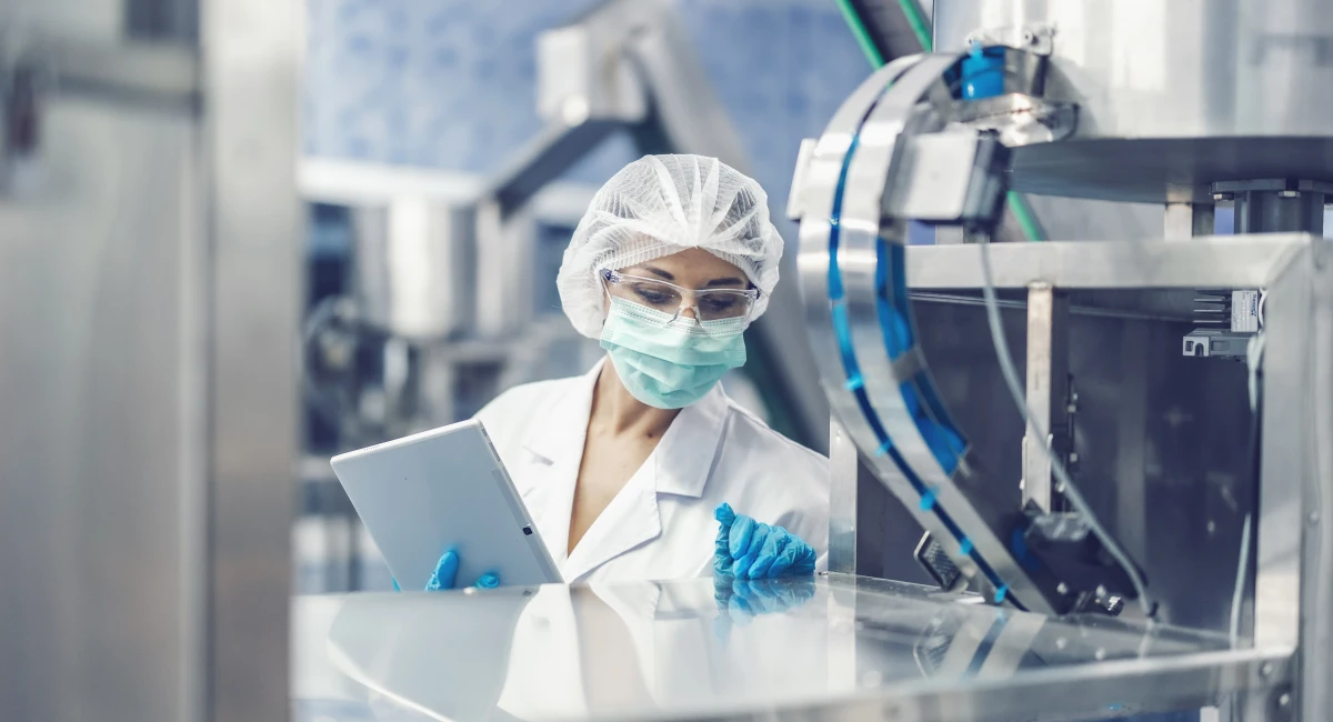 female worker in safety gear looking in to machine in science lab