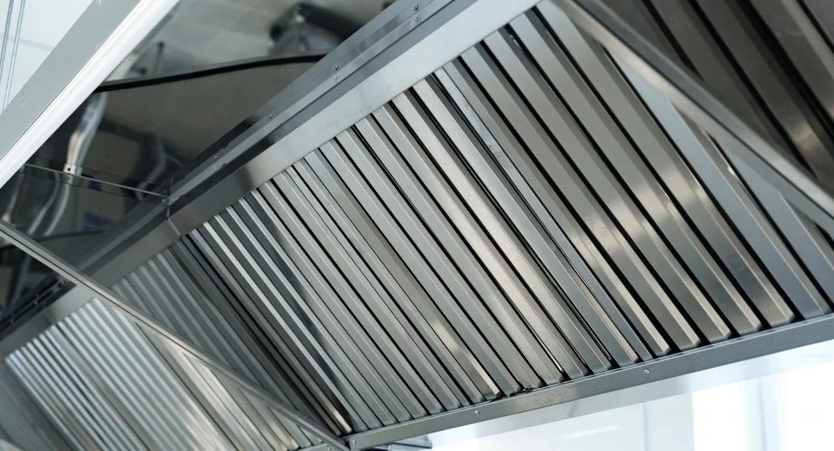 Commercial stainless steel kitchen ventilation hood and grease filter system installed above cooking equipment.