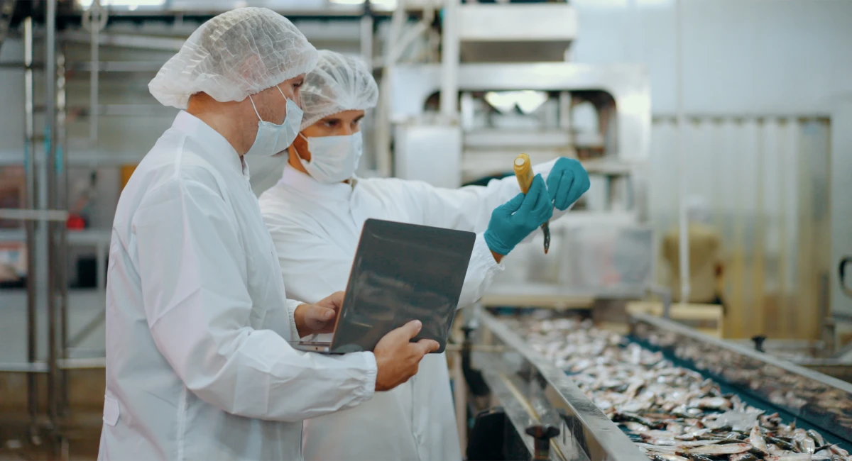 Two food processing workers in protective clothing and face masks inspecting products on a commercial production line.